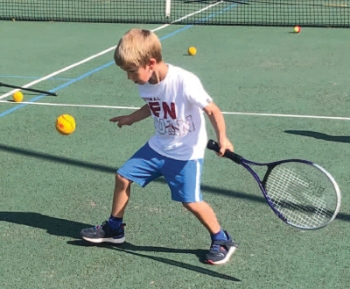 child on a green tennis court learning to play tennis